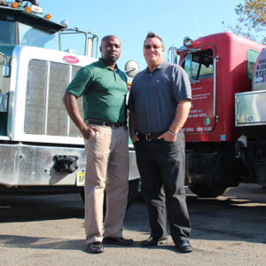 two male employees standing in front of trucks