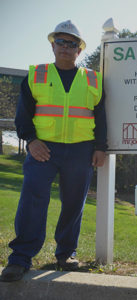 a male employee wearing a safety vest hard hat and safety glasses next to a safety sign