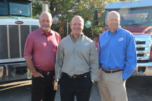 three male executives standing in front of two trucks