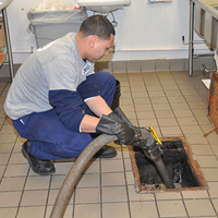 a worker is vacuuming out a grease trap in the floor of a commercial kitchen